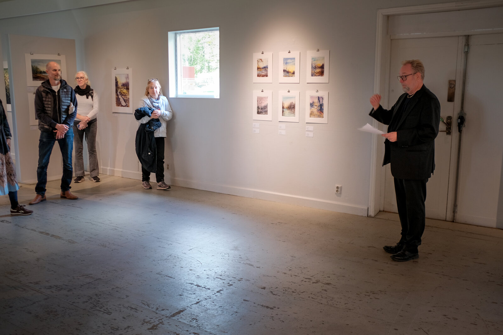 Sven Einarsson läser sitt öppningstal i konsthallen medan besökare lyssnar.