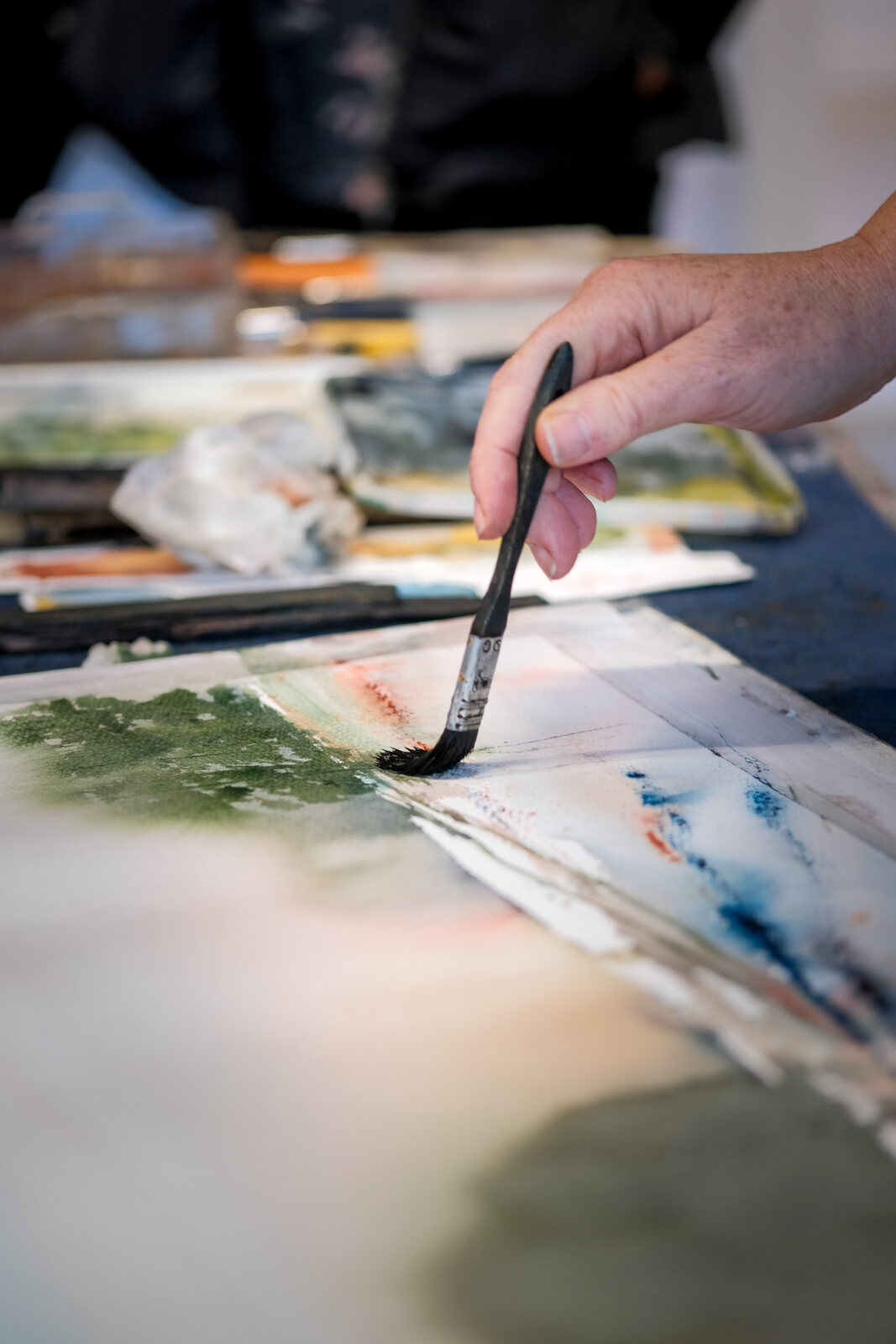 En hand med pensel målar ett grönt träd på ett akvarellark.